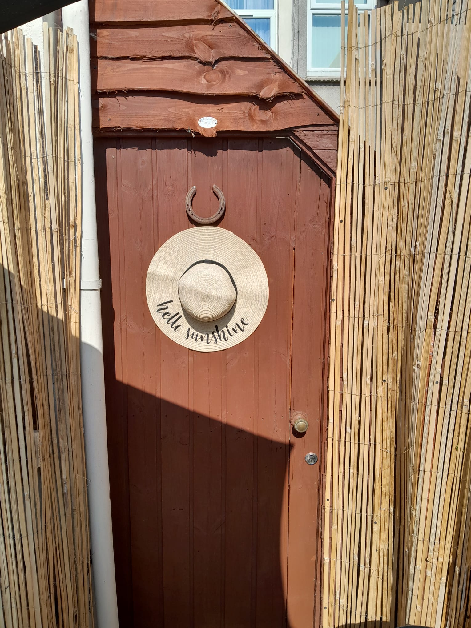 Rustic timber gate with a sun hat and horseshoe framed by bamboo screening